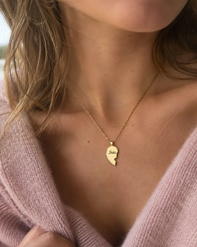 Gros plan sur un morceau de cœur doré gravé Inès, porté avec un pull rose